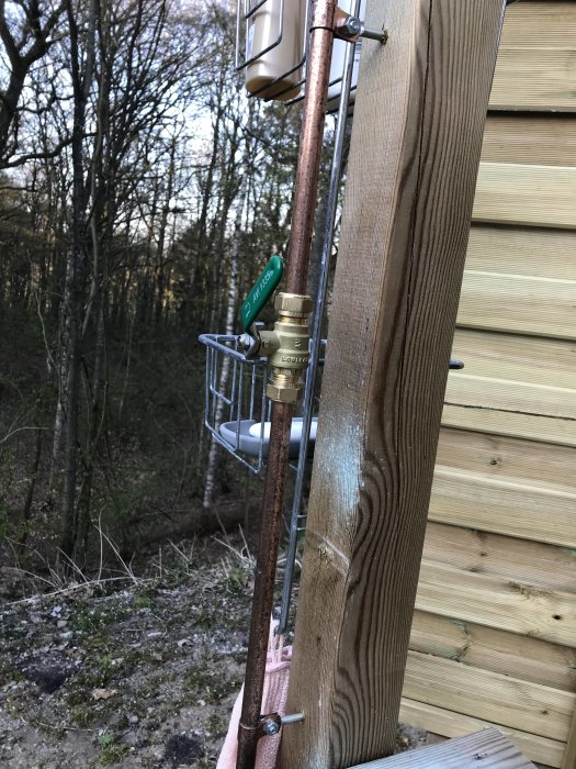 En ny utomhusdusch monterad på en trästolpe med kopparledningar och en duschmunstycke.