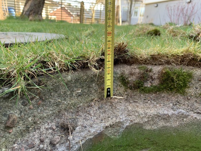 Måttband visar höjden på en öppen stenkista med mossa i trädgården.