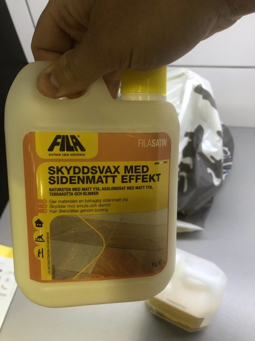 Flaska med skyddsvax för klinkergolv hållen i en hand, märkt "Skyddsvax med sidenmatt effekt".