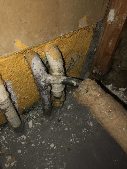 Gamla vattenledningar och -utkastare i en vägg med synliga rör och anslutningar mot en betongplatta.