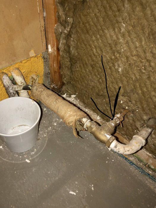 Gammal vattenutkastare med markerat tunt rör, intill isolering och betonggolv under renovering.