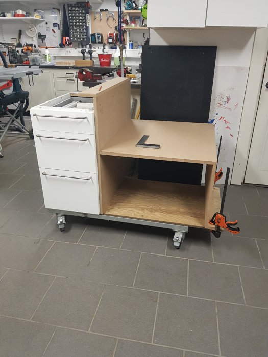 Pågående bygge av en köksö med vit skåpinredning och träbänkskiva i ett verkstad med verktyg i bakgrunden.