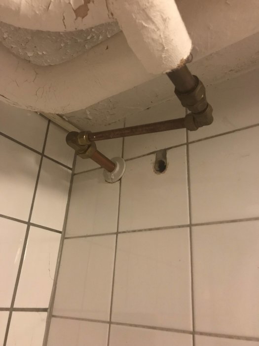 Vattenutkastare som är ansluten till kopparrör i vinkel under vitmålat tak och vita kakelväggar.
