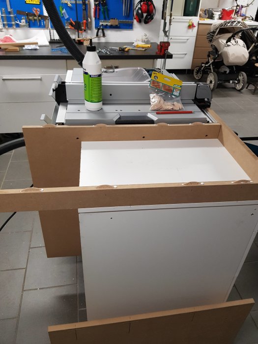 Verkstadsbild med pågående bygge av en vit skåpdel och verktyg i bakgrunden.