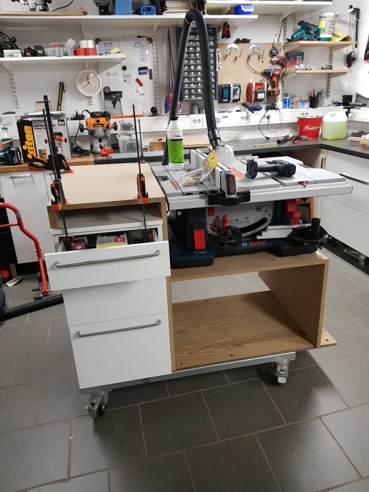 Välorganiserad verkstad med påbörjad tillverkning av en träkonstruktion på ett arbetsbord bland verktyg och utrustning.