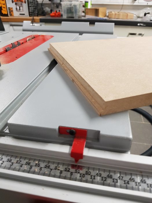Två stycken MDF-skivor på en bordsåg med mätband i förgrunden och verktyg i bakgrunden.