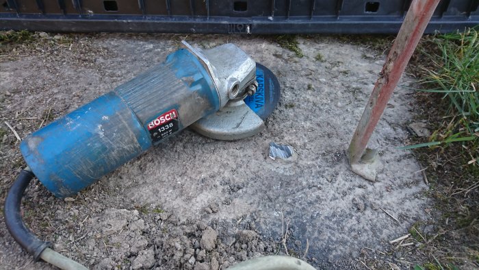 Sliten blå Bosch vinkelslip på marken bredvid en kratta, ris och skräp.