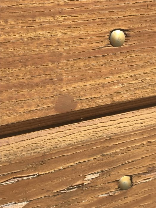 Närbild av träpanel med torkade droppar i mörkare brun nyans och synliga skruvar.