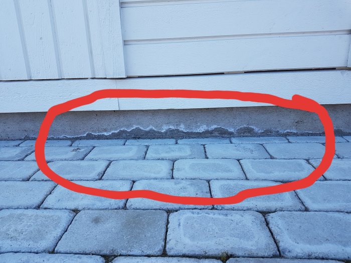 Punaisella ympyröity valkoinen jälki talon sokkelissa, vieressä harmaita kiviä.