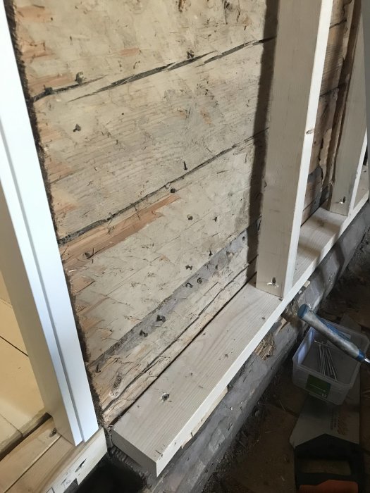 Uppreglad timmervägg nära en dörrkarm, i förberedelse för installation av plywood och gips.