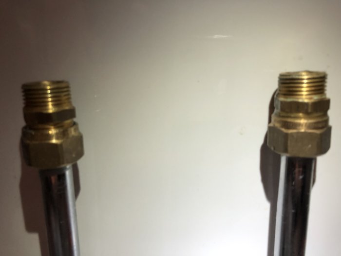 Två förkromade vattenrör med Vatette klämringkopplingar och utvändig gänga mot en vit vägg.