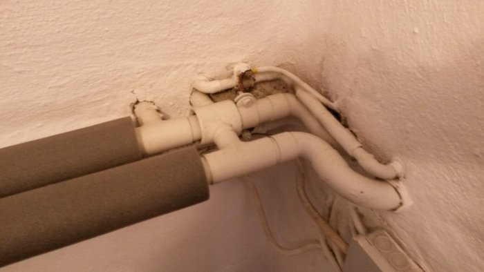 Synliga rörinstallationer anslutna klumpigt med tätningsmassa vid en vit vägg.