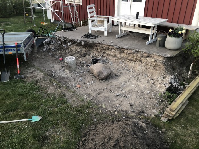Upprivet område för renovering av uteplats med sten, jord och byggmaterial vid husvägg.