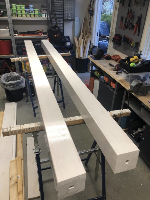 Fyra nymålade, vita räckesstolpar som torkar i en verkstad full med verktyg och byggmaterial.