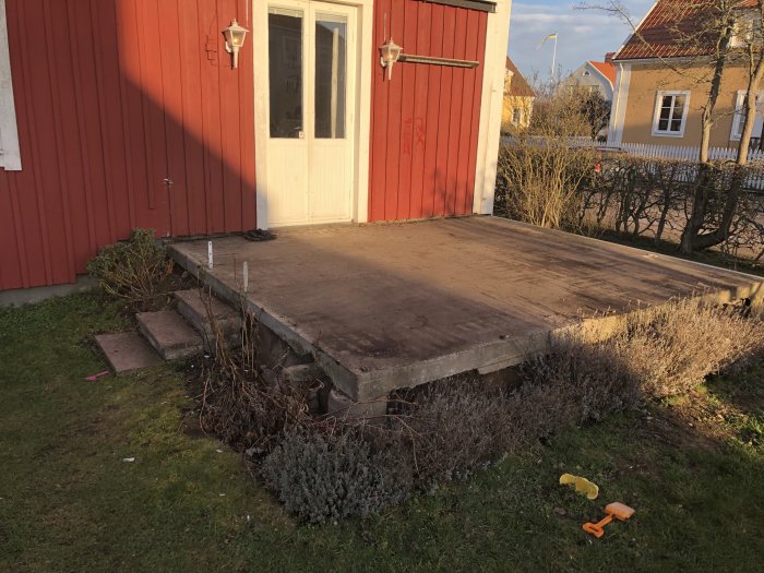 Rivningsfas av en gammal uteplats med betongplatta, synliga stödjande balkar och spår av vegetation.