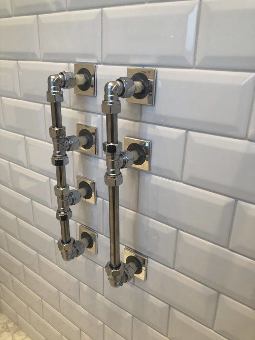 Installerade kromade VVS-rör och ventiler på en kaklad badrumsvägg.