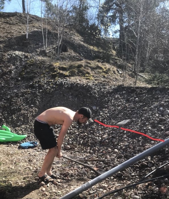 Person gräver vid en rullstensås med markerad röd linje för framtida stödmur.