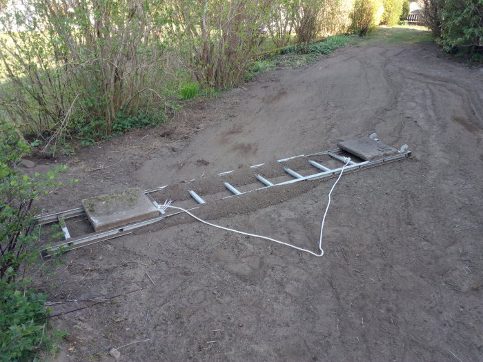 Jordplaneringsstege av aluminium bunden med rep, med en cementplatta på en grusväg för markutjämning.