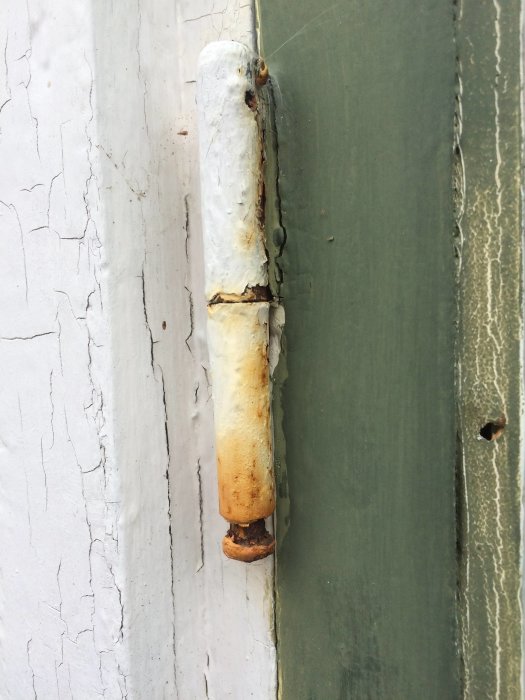Gångjärnspiggen på ett fönster som har glidit ner och behöver justeras, med synlig rost och flagnande färg.