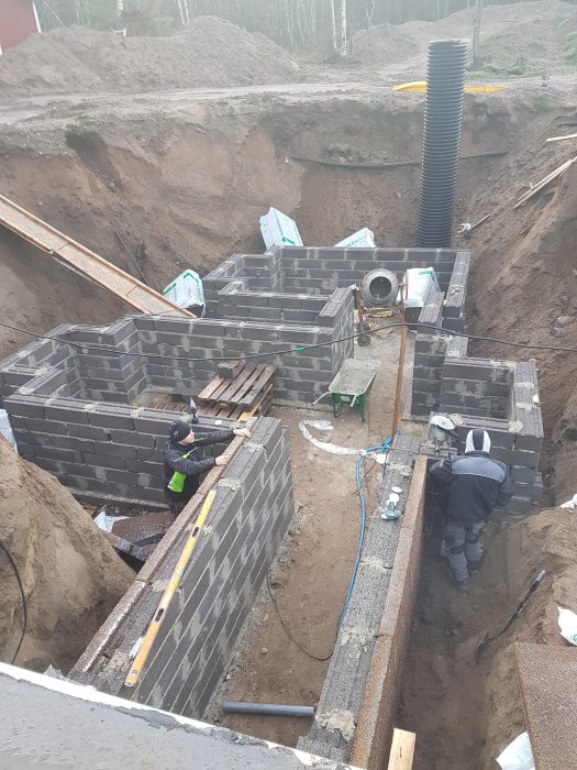 Under construction of an underground wine cellar with workers laying bricks, visible insulation layers, and ventilation pipes.