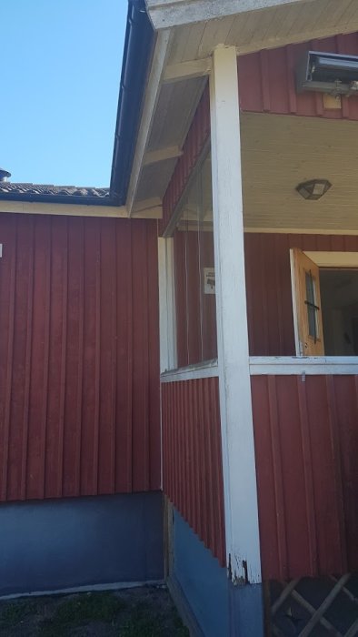 Rød treveranda med rutten bunn av en hvit stolpe. Stolpen støtter taket og har malingsslitasje nederst. Klare himmel i bakgrunnen.