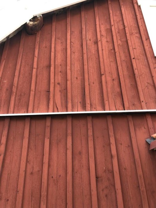 Rödmålad träpanel med torrsprickor och glipor mellan panel och lockläkt på husfasad.