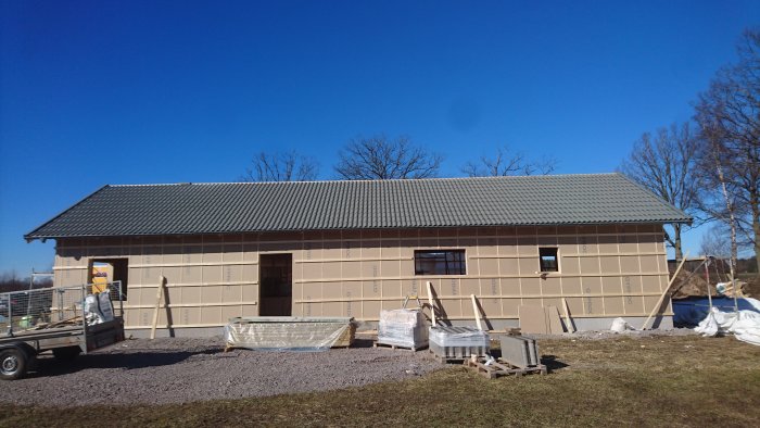 Hus under konstruktion med ytterpanel behandlad med järnvitriol, material på marken och blå himmel.