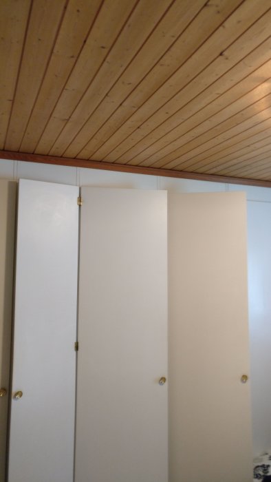 Vit garderobsvägg och paneltak i ett äldre sovrum, färdigt för renovering och målning.