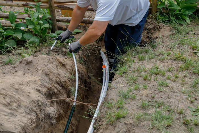 Person gräver en grävtrench och lägger ner elkablar utomhus.