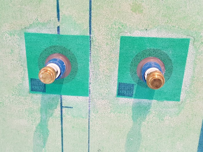 Två kopparrör med blå tejp på ändarna monterade i en vägg täckt med grönt gips.