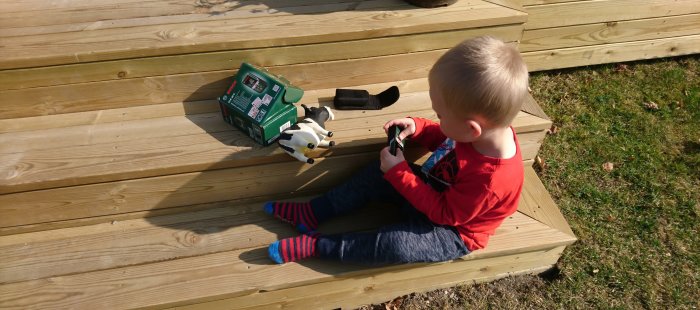 Barn sitter på trätrappa och tittar på Bosch PLR 30 C, leksaksko bredvid kartongen.