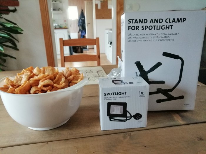 Arbetslampor och förpackning för spotlightstånd på bord, skål med snacks framför.