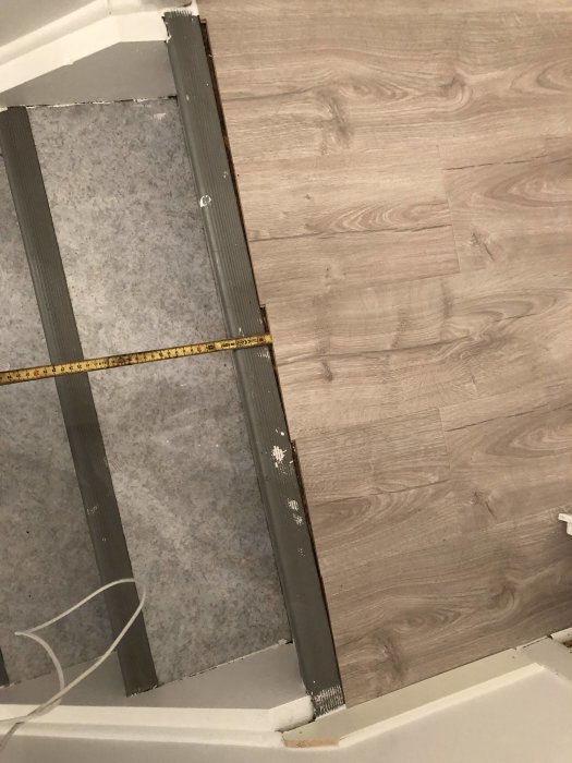 Ofullständigt anslutet laminatgolv vid trappan som behöver en avslutande list, med måttband på golvet.