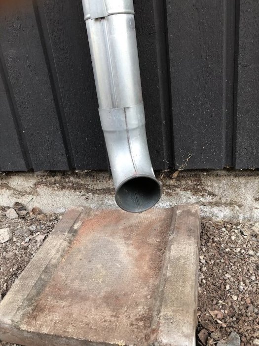 Stuprör som leder ner till marken vid husets hörn med en utkastare över en betongplatta.
