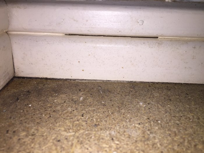 Närbild på en spånskiva vid en vit dörrlist med ventilationshål i källare