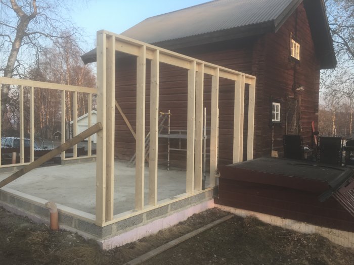 En nästan färdigbyggd trävägg på ett byggprojekt nära ett rödmålat hus med bastu.