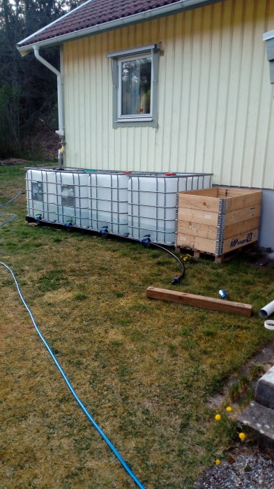 Regnvattensystem med flera ihopkopplade IBC-tankar och blå PEM-kopplingar vid en husvägg.