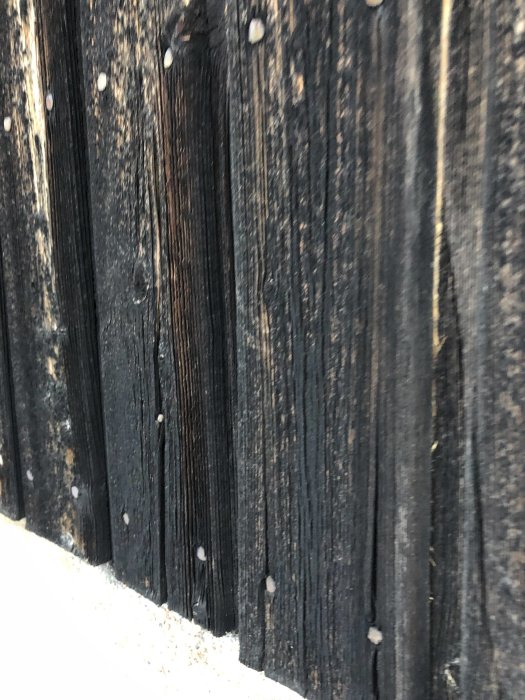 Solbränd, brunmörk träpanel med tydliga tecken på väderpåverkan och slitage.