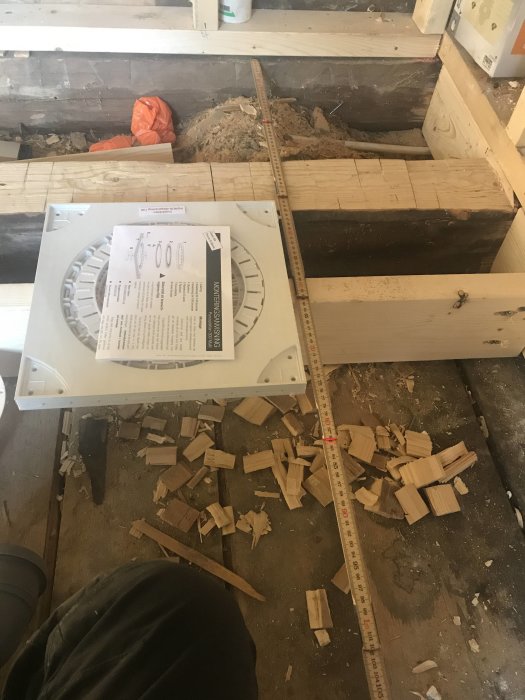 Golvvyer med ett mätband över golvreglar och en duschbrunn placerad vid regeln, omgivet av träspån och bruksanvisning.