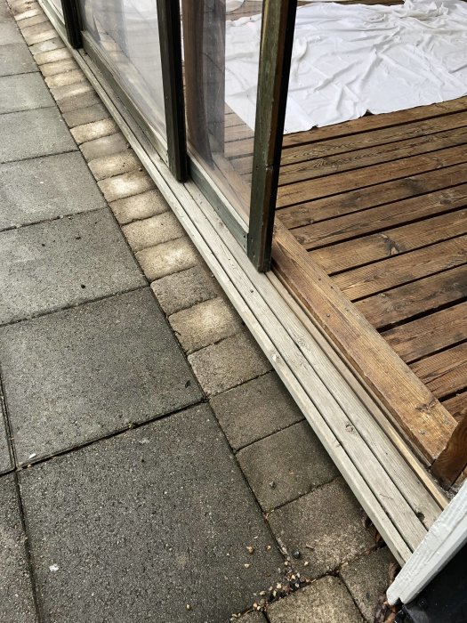 Sliten golvskena och trädörrar med plexiglas i ett uterum mot en trätrall och stenplattor.