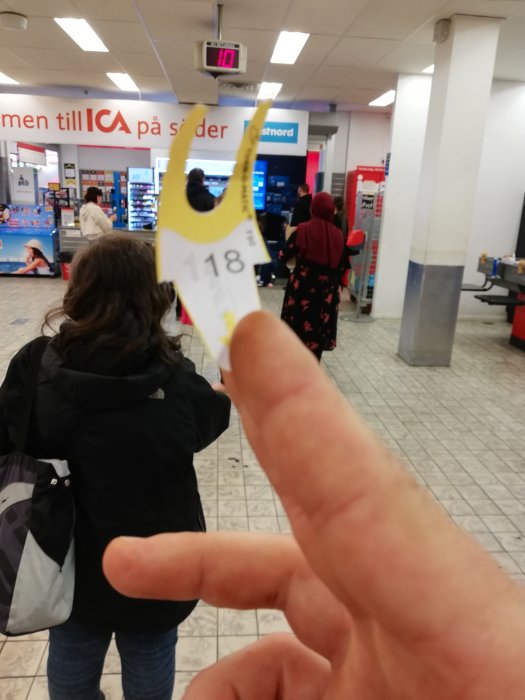 Könummerlapp med siffran 118 hålls upp framför folksamling i butikskö.