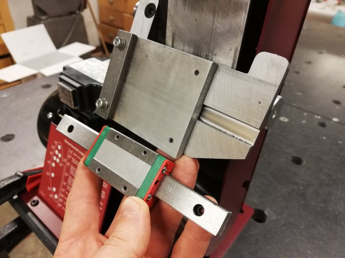 Hand håller ett metalliskt sidostöd med glidfunktion på en röd maskin.