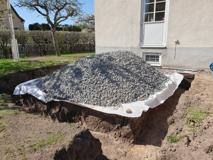 Hög med grus bredvid uppgrävd mark vid ett hus för pågående byggprojekt.