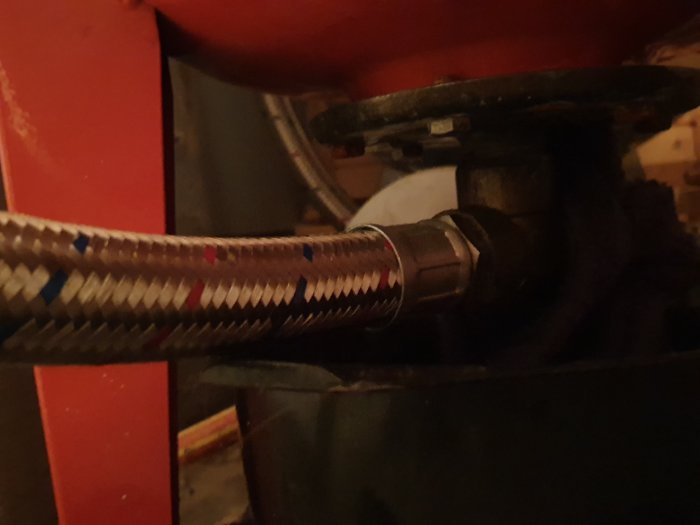 Värmesystem med flexibel slanganslutning till en rödmålad rörledning.
