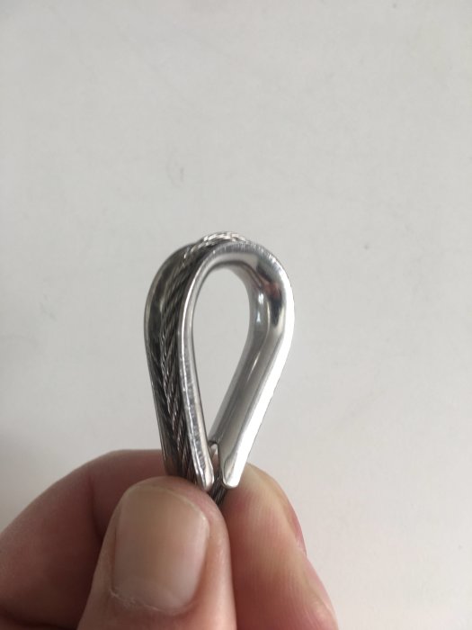 En person håller en metallkaus fäst på en metallvajer, vilket indikerar användning inom bygg.