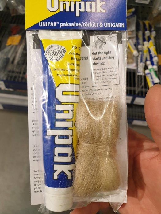 Hand håller ett paket med Unipak paksalve och linhampaprodukter för rörmokeri.