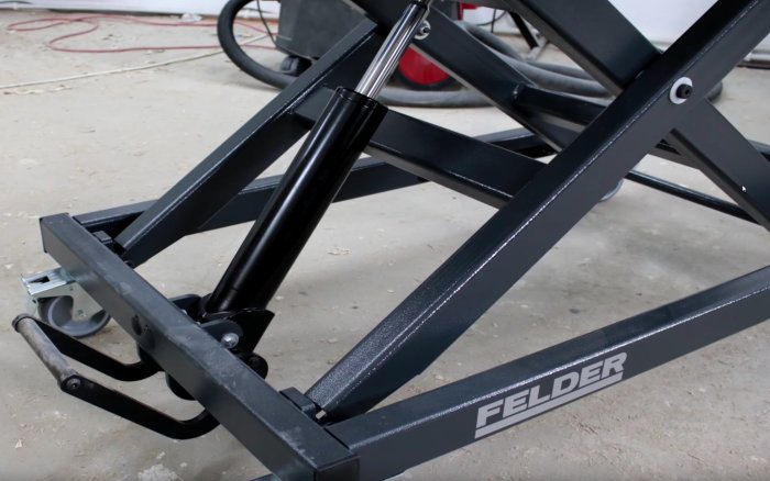 Närbild på svart metallställning med hydraulcylinder och länkhjul, potentiellt för byggprojekt.