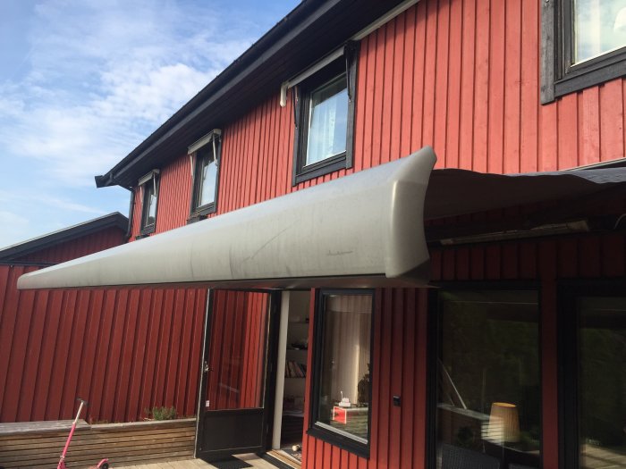 Upprullad markis med solblekning på ett rött hus med svarta fönsterkarmar.