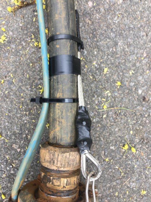 Reparationsarbete på brunnspump med sågad krok, tejpad slang och kopplingar på marken.