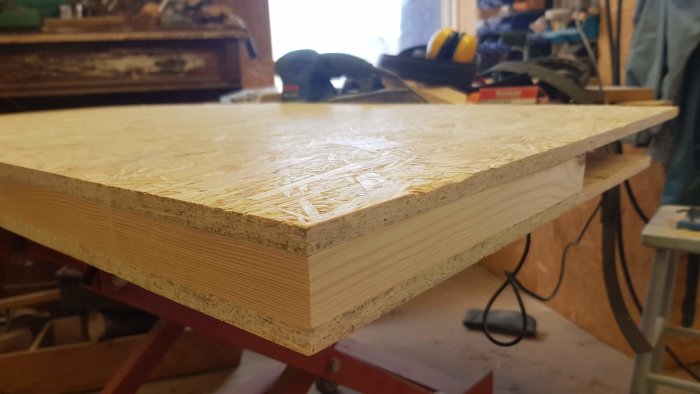 Hörn av hemmagjord träram utan synliga skarvar med limmad OSB-skiva ovanpå i en verkstad.
